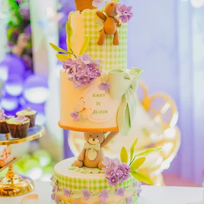 I believe the dessert table should be as beautiful as the main decor. Here, I've styled a stunning multi-tiered 'Baby in Bloom' cake, ensuring it perfectly matches the green gingham and lavender floral theme of the celebration.