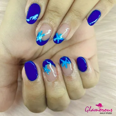 A beautiful mix of solid and negative space design. This manicure features a bold, electric blue polish with accent nails showcasing a sheer base and a blue floral design.
