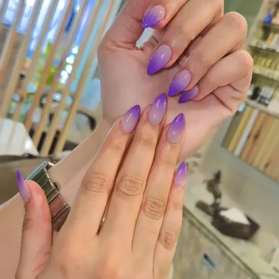 A beautiful purple ombre on sharp stiletto nails. The color fades perfectly from a sheer nude at the base to a vibrant violet at the tip for a striking and elegant look.