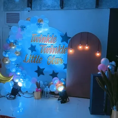 A closer look at our "Twinkle Twinkle Little Star" decor. This setup features custom gold lettering against a blue-lit backdrop, surrounded by a cloud of white and blue balloons and accented with a crescent moon prop.