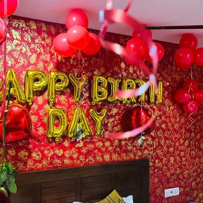 A romantic birthday surprise we set up in a hotel room. The decor features gold "Happy Birthday" foil balloons against a rich red and gold wallpaper, with red balloons and ribbons floating on the ceiling.