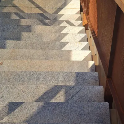 A simple composition of stone, metal, and sun. The sharp, rhythmic shadows cast by the railing create a dynamic pattern on the granite steps, transforming a simple staircase into a canvas for light.