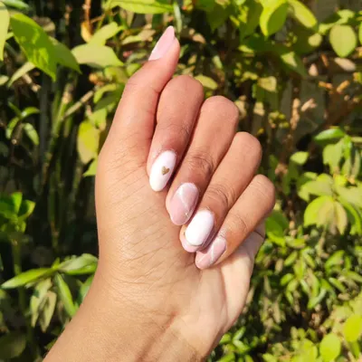 A soft and elegant gel polish set on natural nails. This design features a mix of solid white, a pink marble effect, and a tiny gold heart accent. It's a beautiful example of minimalist nail art.