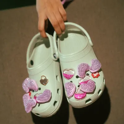 A creative product-focused shot for Crocs. Holding the shoes up to the camera highlights the customizable Jibbitz charms, showing the fun and personalizable aspect of the product.