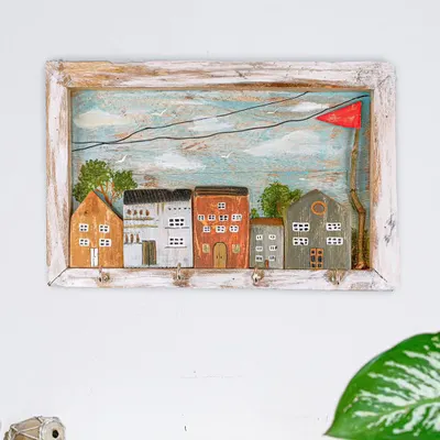 A functional piece of art, this keyholder features a hand-painted scene of miniature houses. It's crafted from wood with a rustic frame, perfect for keeping your keys organized in style.