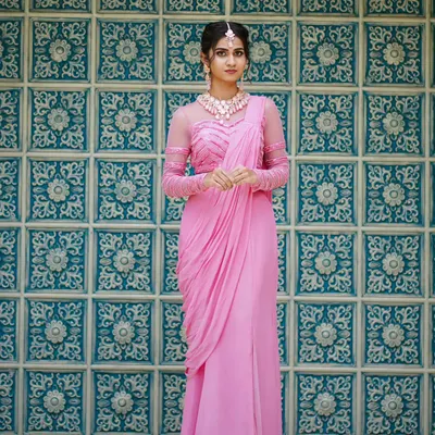 A full-length view of our elegant pink pre-draped saree. The outfit features a stylish blouse with sheer, embellished sleeves and a gracefully draped pallu for a modern silhouette.
