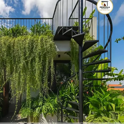 A sleek black spiral staircase provides access to a rooftop garden, surrounded by lush greenery. Its compact footprint preserves valuable space while adding a modern, sculptural element to the verdant setting.