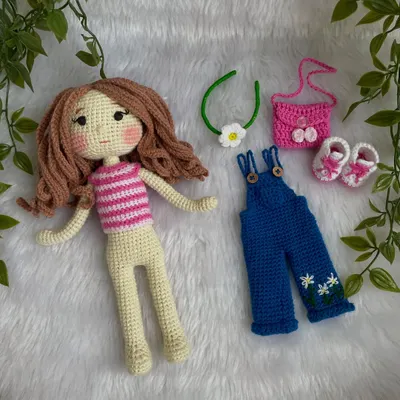 This doll is all ready for playtime with her full set of removable clothes. The set includes a striped top, blue overalls with daisy embroidery, pink shoes, a matching bag, and a flower headband.