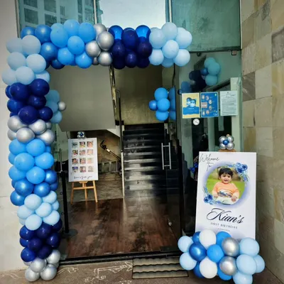 A welcoming entrance for Kian's first birthday. The blue and silver balloon arch, personalized welcome sign, and milestone photo board create a beautiful and personal first impression for guests.