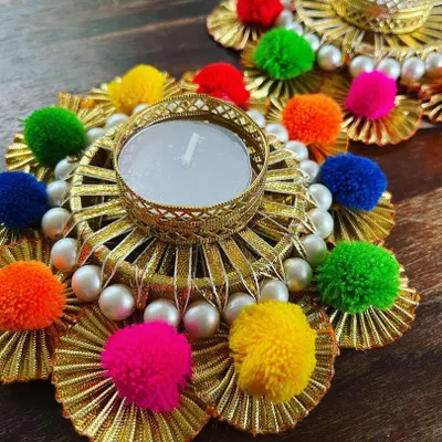 We are all about adding that festive vibe to your home. This is a close-up of our handmade tea light holder, decorated with gota patti, bright pompoms, and delicate pearls, perfect for your Diwali decor.
