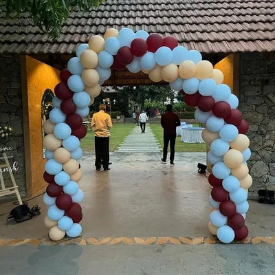 A beautiful organic balloon arch in muted tones of maroon, beige, and light blue, creating an elegant entrance for an outdoor event.