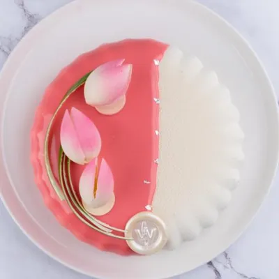 A modern and artistic cake design featuring a glossy pink glaze and delicate, handcrafted sugar tulips. The other half of the cake has a textured white finish, creating a beautiful contrast for a chic and elegant event.