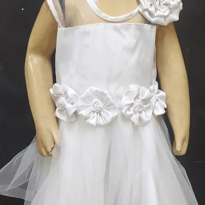 A beautiful white party frock for a child, designed and stitched by one of our students. The dress features a net overlay, sheer shoulders, and handmade satin flowers on the waist and shoulder, demonstrating skills in both sewing and embellishment.