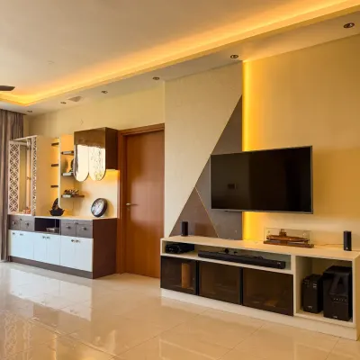 A beautifully lit living room featuring warm cove lighting above the TV unit and accent lights in the shelving. The entire setup is automated for mood control.
