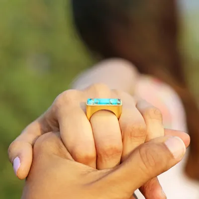 A lifestyle shot that tells a story. By showing the model's hand held by another, the focus on the turquoise statement ring becomes about connection, making it more than just a product photo.