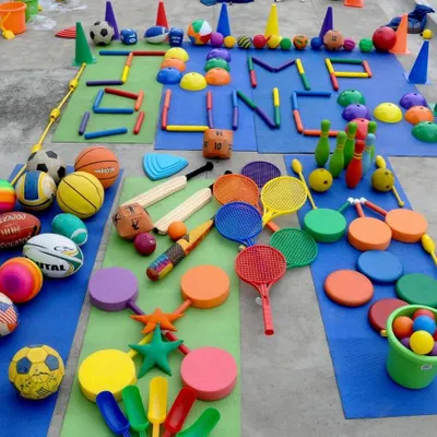 A vibrant display of the diverse sports equipment I use, from basketballs and cricket bats to agility markers and bowling pins. This collection allows me to tailor activities to any age group and skill level, ensuring no two sessions are ever the same.
