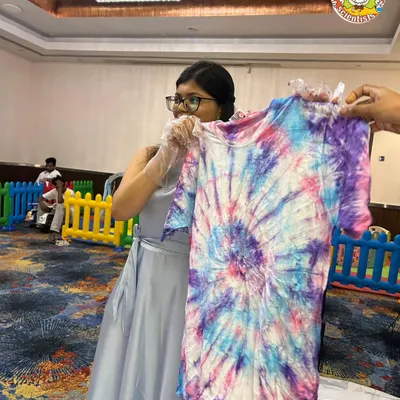The big reveal. A student proudly displays her finished tie-dye T-shirt, a vibrant explosion of color created during one of our corporate event workshops.