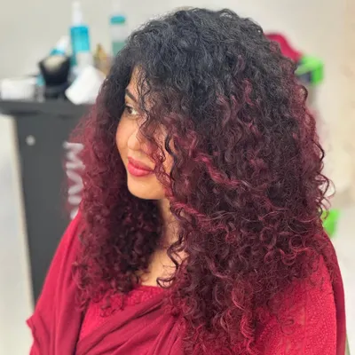 A full view of this stunning red balayage on long, beautiful curls. The color is strategically placed to create dimension and movement, making the curls pop. This shows how vibrant color can work in harmony with natural texture.