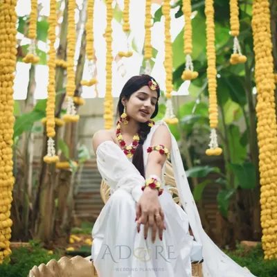 A beautiful bride enjoying her Haldi ceremony. The backdrop of hanging yellow chrysanthemums and lush greenery creates a vibrant and joyful atmosphere, perfect for this pre-wedding ritual.