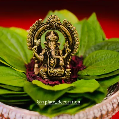 A close-up of a Ganesha idol, the remover of obstacles, resting on a bed of betel leaves. This kind of simple, elegant pooja arrangement is perfect for inviting blessings into your new home.