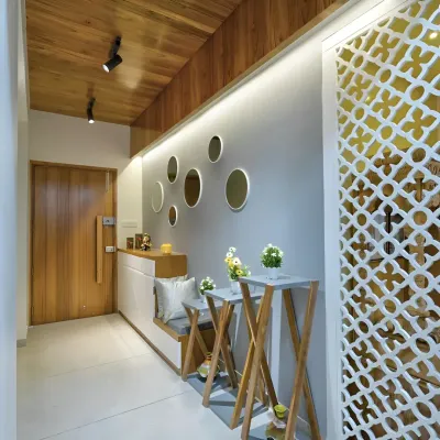 A bright and welcoming foyer design featuring a wooden ceiling, a built-in bench with storage, and a decorative jali partition. The circular mirrors and plant stands add a touch of modern elegance.