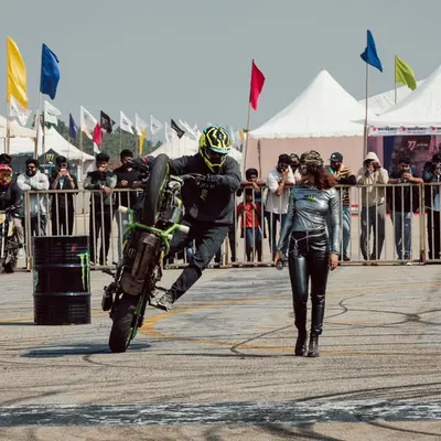 A professional stunt rider performs a wheelie in the stunt zone, surrounded by an engaged crowd and Monster Energy branding. This is brand activation at its most exciting.