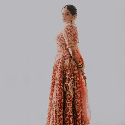 A full-length portrait showcasing a royal red bridal lehenga. The makeup is designed to be comfortable and long-lasting, carrying the bride beautifully through her entire wedding night.