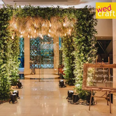 The grand entrance for Rucha and Chinmay's Sangeet night. A lush tropical green archway with a ceiling of golden palm leaves and warm Edison bulbs set the perfect mood.