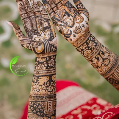 A full view of a stunning bridal mehendi, showcasing intricate patterns from the elbow down. The design features portraits, peacocks, elephants, and beautiful floral bands.