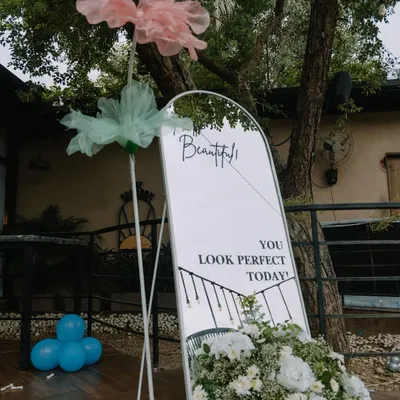 A chic welcome setup for a Dior-themed baby shower. The arched mirror features custom lettering and is anchored by a beautiful arrangement of white peonies and greenery, creating an elegant entrance.