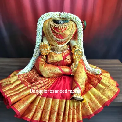 This is the quintessential result of my full draping service. The rich red silk saree is draped to create a grand, circular base, and the idol is fully adorned for the Varamahalakshmi festival.