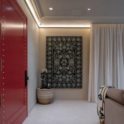 A bold, brass-detailed red door makes a powerful statement in this living room. I contrasted it with a hand-embroidered wall panel and lime-plastered walls, layering global artifacts to create a contemporary space that is both warm and culturally rich.
