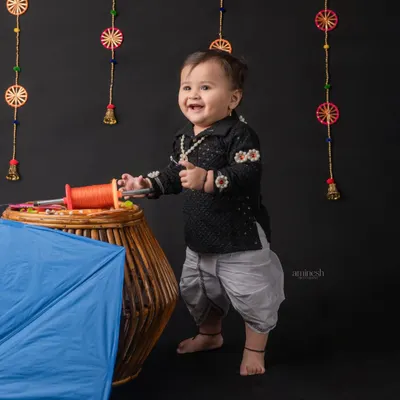A joyful baby boy in a traditional black kurta for a Makar Sankranti shoot. He stands by a basket of kite string, ready to celebrate the kite flying festival with a big smile.
