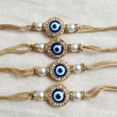 Protect your brother from 'buri nazar' with these classic evil eye rakhis. The design features a striking blue and white evil eye charm, surrounded by small crystals and set on a simple jute thread with pearl beads for an elegant touch.
