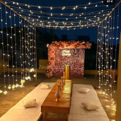 A beautiful terrace dining setup perfect for a romantic evening. This arrangement features a canopy of fairy lights, low seating with comfortable cushions, and a decorated backdrop, creating a private and magical atmosphere under the stars.
