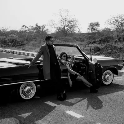 A classic black and white shot from a vintage-themed pre-wedding shoot. The convertible car and the couple's stylish outfits create a timeless, cinematic feel that is both cool and romantic.