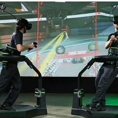 Two players work together in a multiplayer game on the Virtuix Omni treadmills. This setup encourages communication and strategy, making it an effective and exciting tool for corporate team-building workshops.
