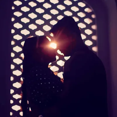 A beautiful silhouette of a couple with the sun flaring between them, framed by an intricate jaali window.