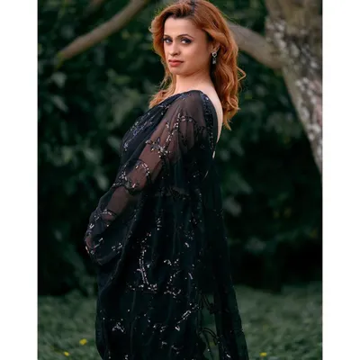 An elegant outdoor portrait of a woman in a beautiful black saree. The natural green background provides a perfect contrast, making the subject stand out.