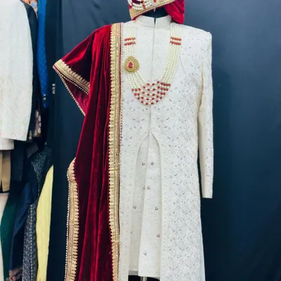 A full view of a trending floral hand-detailed sherwani. This ivory piece is paired with a rich red velvet dupatta, a custom turban, and a pearl necklace, creating a complete and majestic groom's ensemble.