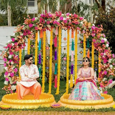 A cool and quirky Haldi portrait, with the couple wearing sunglasses against a stunning floral and tassel backdrop.