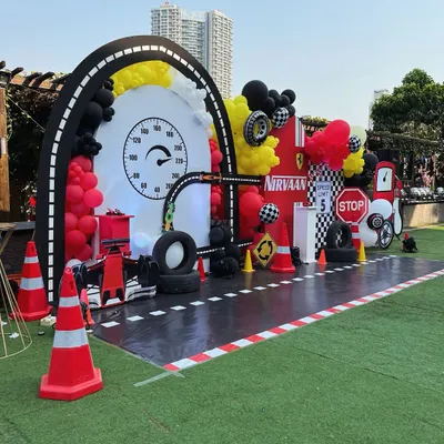 Ready, set, go! A full-throttle race car party setup with a custom track, a speedometer backdrop, and tons of themed props like tires, traffic cones, and a fuel station.