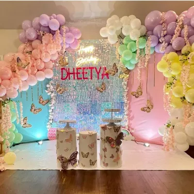 A dreamy butterfly theme with a shimmering sequin backdrop and a rainbow of pastel balloons. This setup for Dheetya's birthday includes custom butterfly-themed pedestals and hanging floral elements for an ethereal feel.