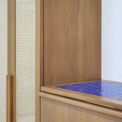 A detail showing the junction of materials in a custom furniture piece. The warmth of the wood and cane is punctuated by a surprising pop of vibrant blue tile, creating a unique and playful accent.