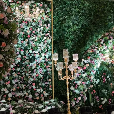 A close-up of a lush floral wall, showing the rich texture created by mixing different types of flowers and greenery, accented by an elegant candelabra.