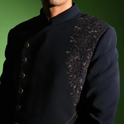 A close up of the dark navy asymmetric jacket, focusing on the intricate leaf embroidery that cascades down one side. This detail adds a touch of organic artistry to the sharp, structured design of the jacket.