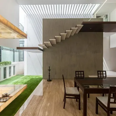 an open-plan space featuring a floating puja unit in backlit onyx, juxtaposed with a minimalist wooden dining set and a cantilevered staircase… a dialogue between spiritual and social spaces.