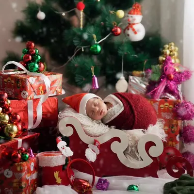 A peaceful newborn sleeping in a miniature sleigh, surrounded by Christmas gifts and decorations. This is a perfect example of a themed newborn session.