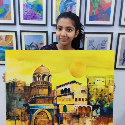 A student proudly displays her large-scale acrylic painting of a historic Indian city, bathed in a warm, golden light. This piece showcases advanced skills in architectural detail and color blending.