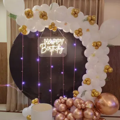 A sophisticated decoration featuring a black circular backdrop. I framed it with a white, rose gold, and gold balloon arch and added a "Happy Birthday" neon sign with hanging fairy lights.